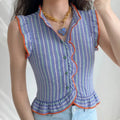 Lifestyle model wearing blue vertical stripe sleeveless blouse, orange contrast ruffle piping trim, stand ruffle collar, asymmetrical ruffle front placket with green round buttons, wing ruffle armholes, fitted peplum hem, matched light blue jeans and heart pendant necklace outfit display