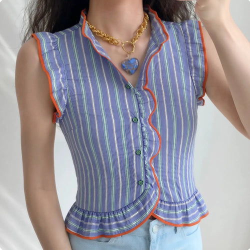 Lifestyle model wearing blue vertical stripe sleeveless blouse, orange contrast ruffle piping trim, stand ruffle collar, asymmetrical ruffle front placket with green round buttons, wing ruffle armholes, fitted peplum hem, matched light blue jeans and heart pendant necklace outfit display