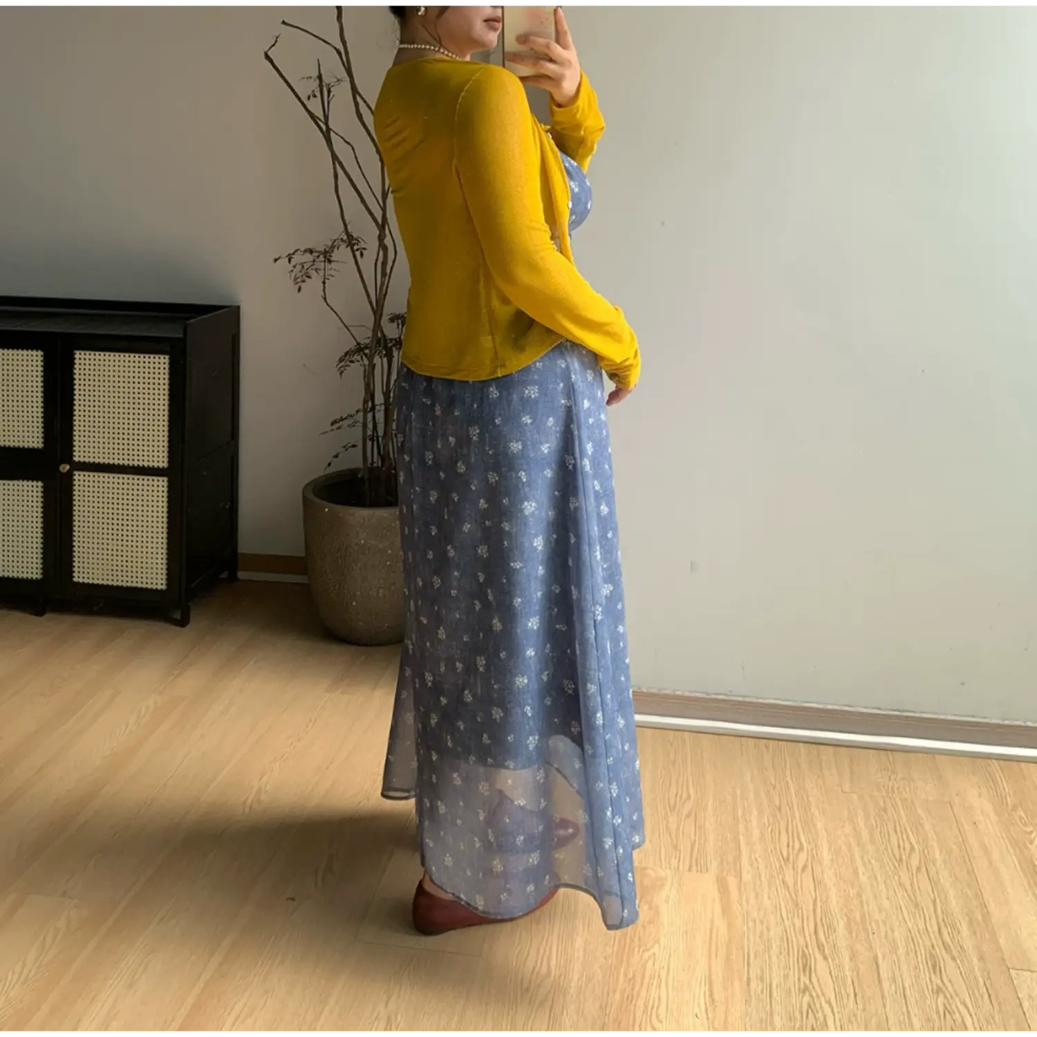 Three-quarter side back indoor mirror shot of denim blue ditsy floral maxi slip dress, layered bright yellow cropped knit cardigan, showing flowy sheer floor-length skirt hem