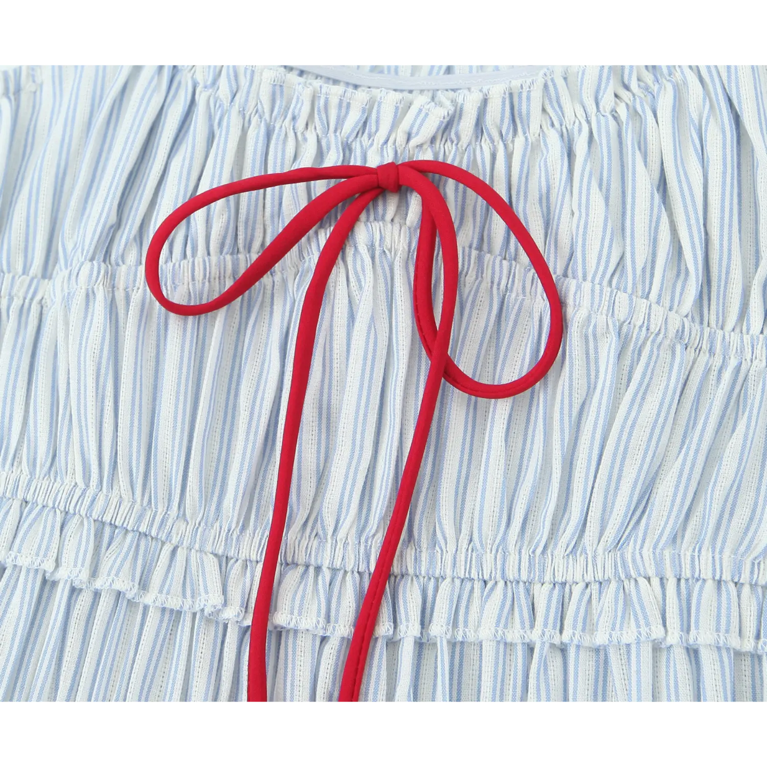 Close‑up bright red self tie bow detail, contrast red string on blue‑white vertical stripe smocked dress