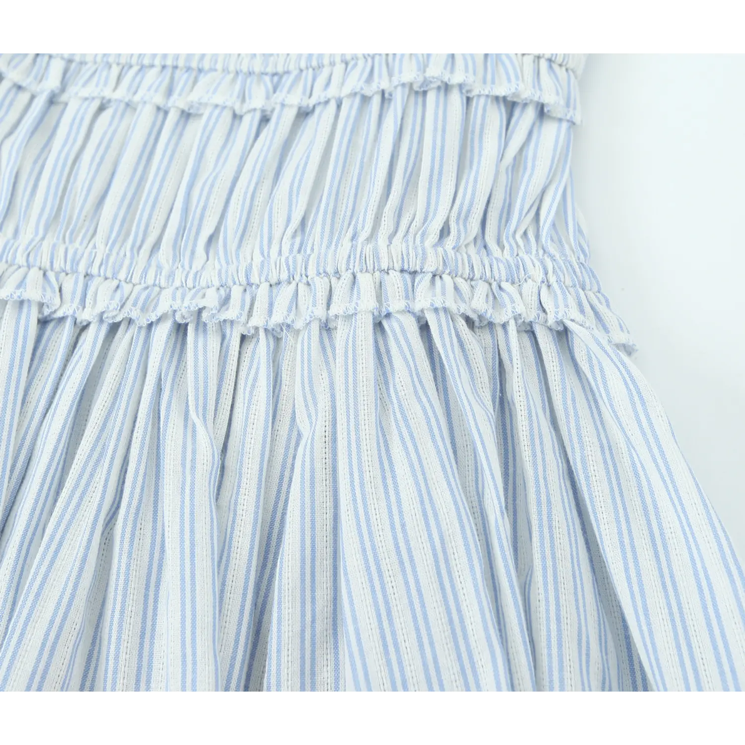 Close‑up view of elastic smocked tier ruffle seam, blue‑white vertical stripe lightweight fabric