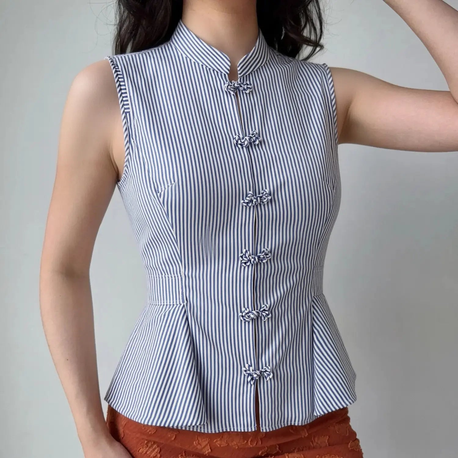 Front lifestyle shot on model of fitted chinese style sleeveless vest top, stand collar, frog buttons, flared peplum hem