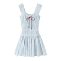 Front view blue white vertical stripe mini dress, smocked tiered bodice, ruffle shoulder straps, red front bow tie, flare skirt, white background