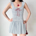 Model wearing blue‑white vertical stripe smocked mini dress, square neck, ruffle straps, contrast red front bow tie, flare short skirt, studio background