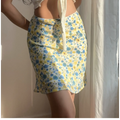 Close-up view of a blue and yellow floral chiffon mini skirt, showing the delicate print and lace-trimmed waistband, paired with a white cropped top.
