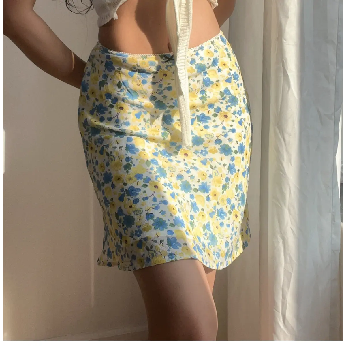 Close-up view of a blue and yellow floral chiffon mini skirt, showing the delicate print and lace-trimmed waistband, paired with a white cropped top.
