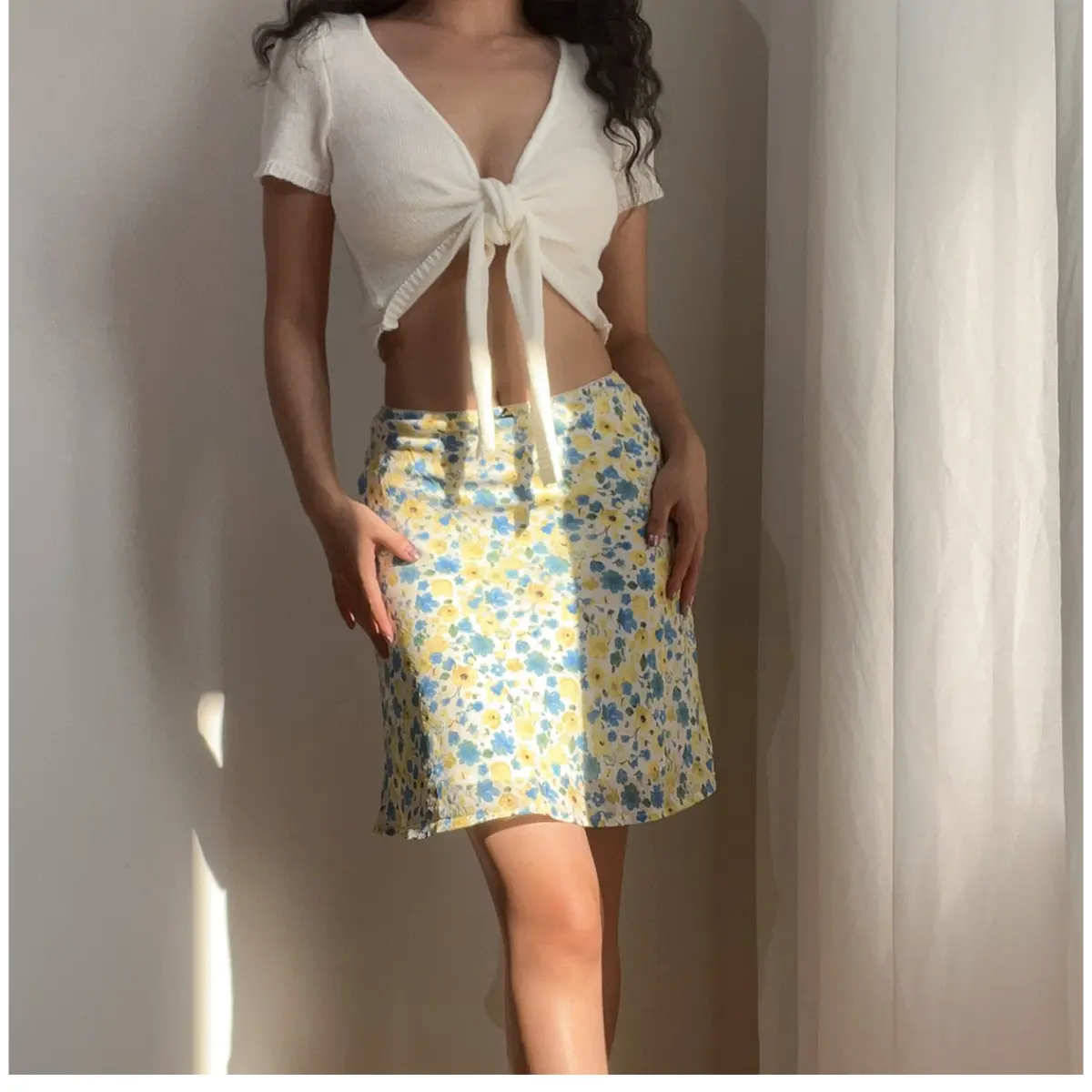 Full front view of a woman wearing a blue and yellow floral chiffon mini skirt, paired with a white cropped knit top, showing the full print and silhouette.
