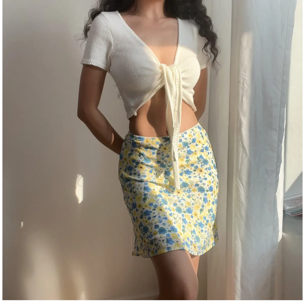 Woman wearing a blue and yellow floral chiffon mini skirt, paired with a white cropped knit top, showing the skirt's flowy silhouette.
