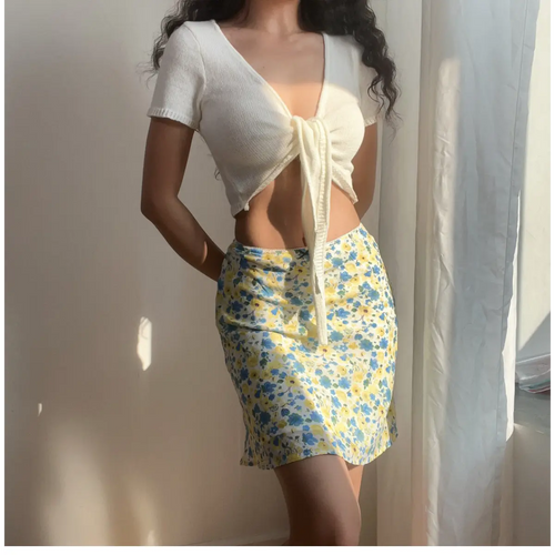 Woman wearing a blue and yellow floral chiffon mini skirt, paired with a white cropped knit top, showing the skirt's flowy silhouette.
