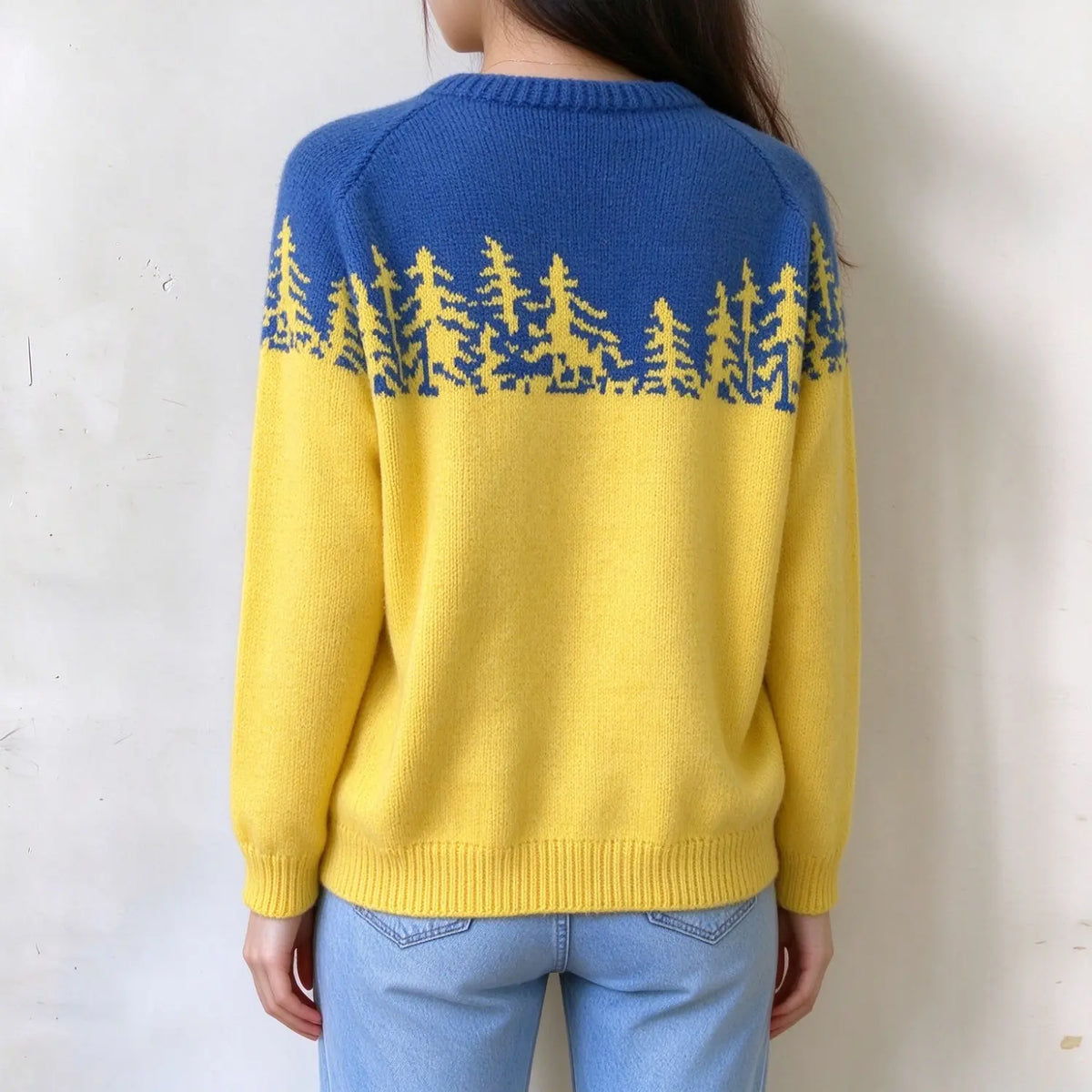 Female model back view, two-tone blue and yellow fairisle knit sweater, pine tree jacquard pattern on upper yoke, ribbed crew neck and hem