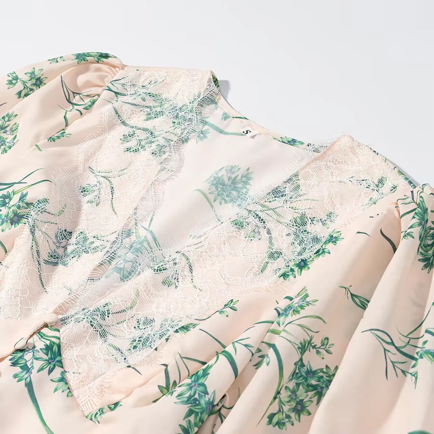 Close‑up shot of white lace v‑neck neckline and puff shoulder with green floral print fabric