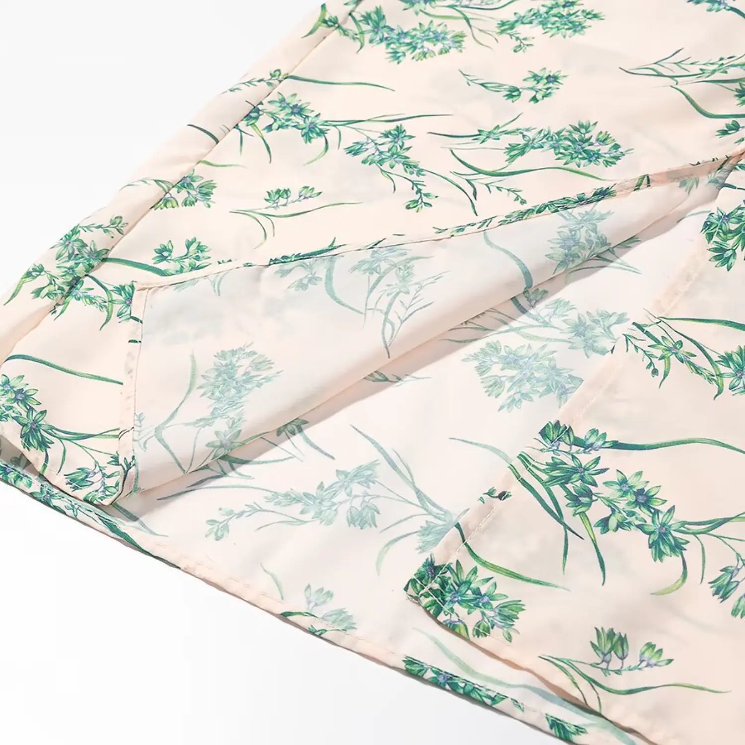 Close‑up view of skirt hem, inner slit and stitching on blush green floral midi dress