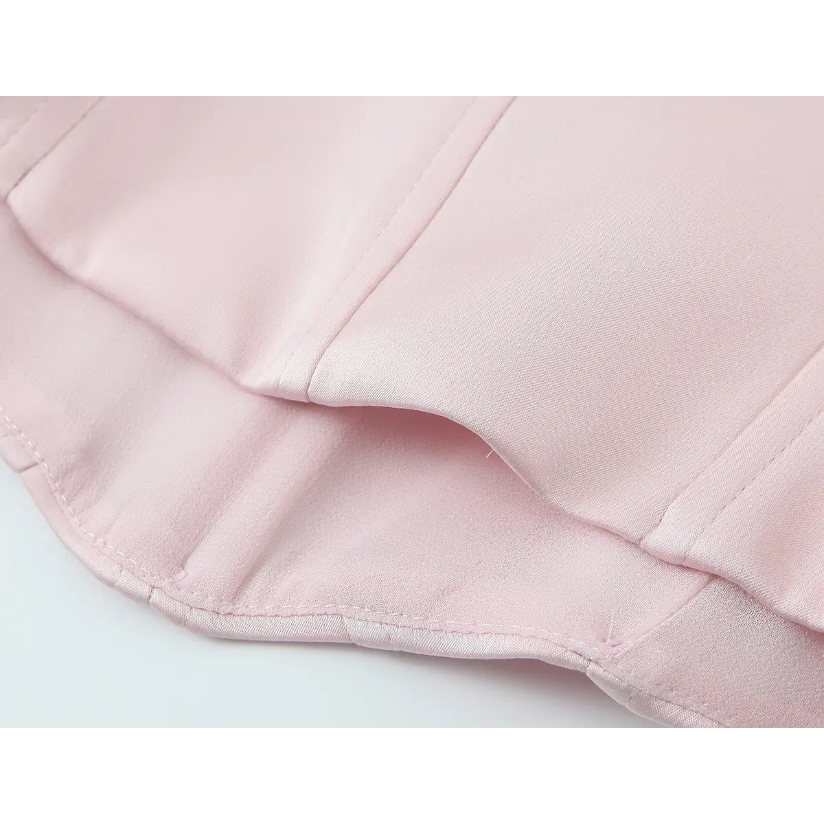 Close-up of the hem on the blush pink bustier top, showing the double-layered construction and smooth, matte fabric finish
