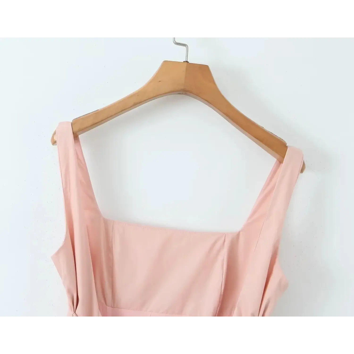 Close‑up of blush pink mini dress square neckline with wide shoulder straps hanging on wooden hanger, clean tailored seam detail