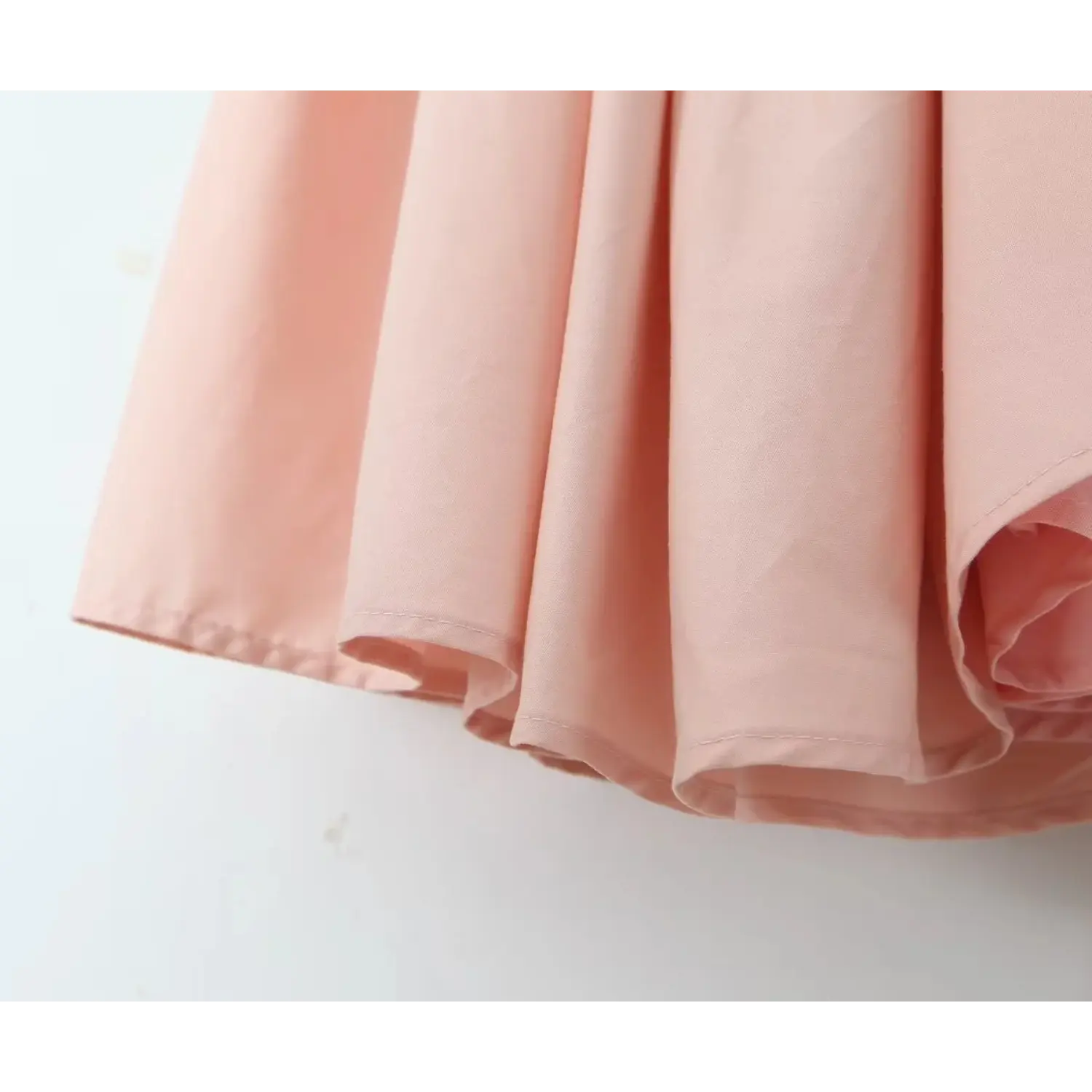 Close‑up dress hem, clean finished stitching, smooth blush pink fabric, full flared skirt edge view