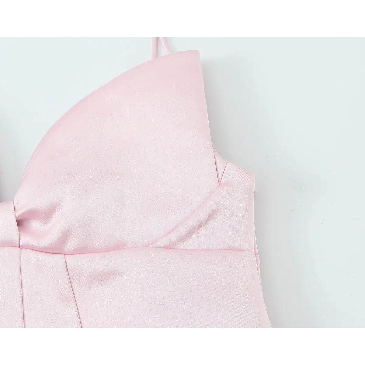 Close-up view of the structured bust on a blush pink satin mini dress, showing the central knot detail and thin spaghetti straps.