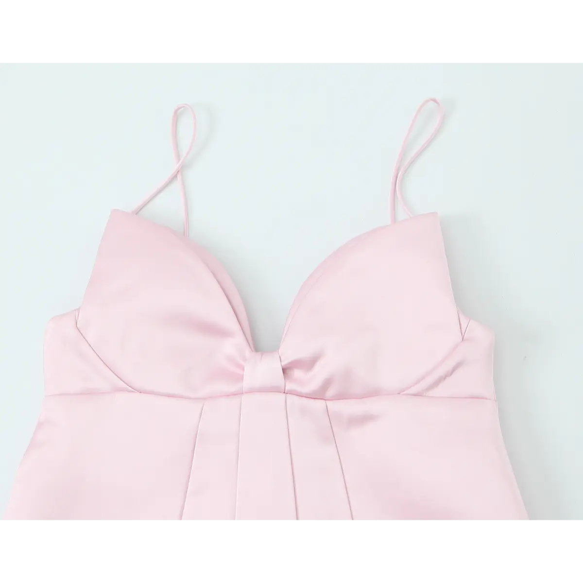 Full front view of a blush pink satin mini dress, showcasing the structured bust, central knot, thin straps, and pleated skirt.