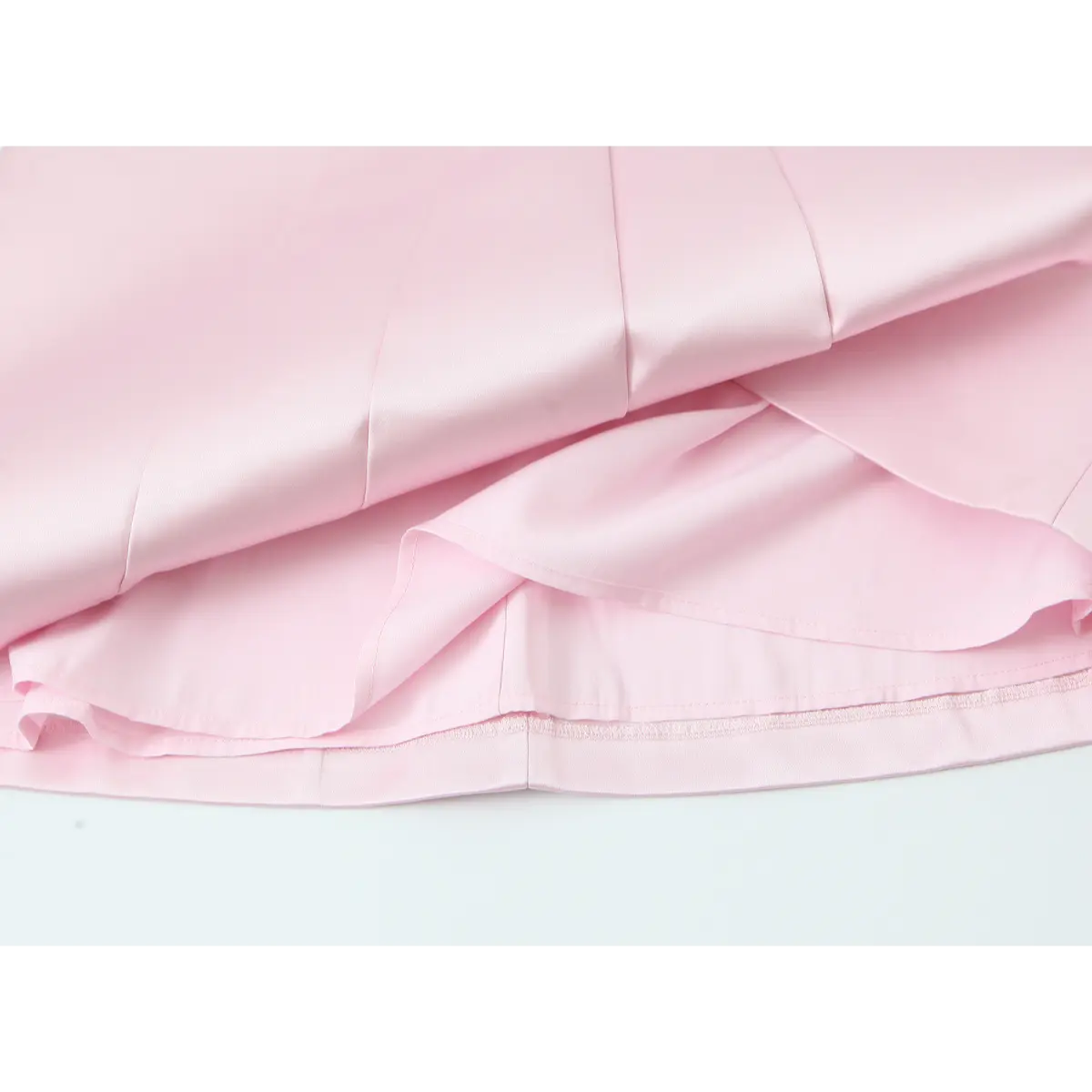 Close-up detail shot of the skirt lining and pleats on a blush pink satin mini dress, showing the double-layer construction.
