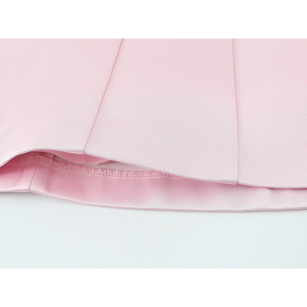 Close-up detail shot of the skirt pleats and lining on a blush pink satin mini dress, showing the neat stitching.