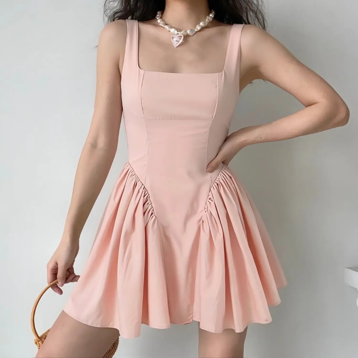 Female model wearing blush pink square neck mini skater dress, fitted waist, voluminous gathered flare skirt, casual elegant styling