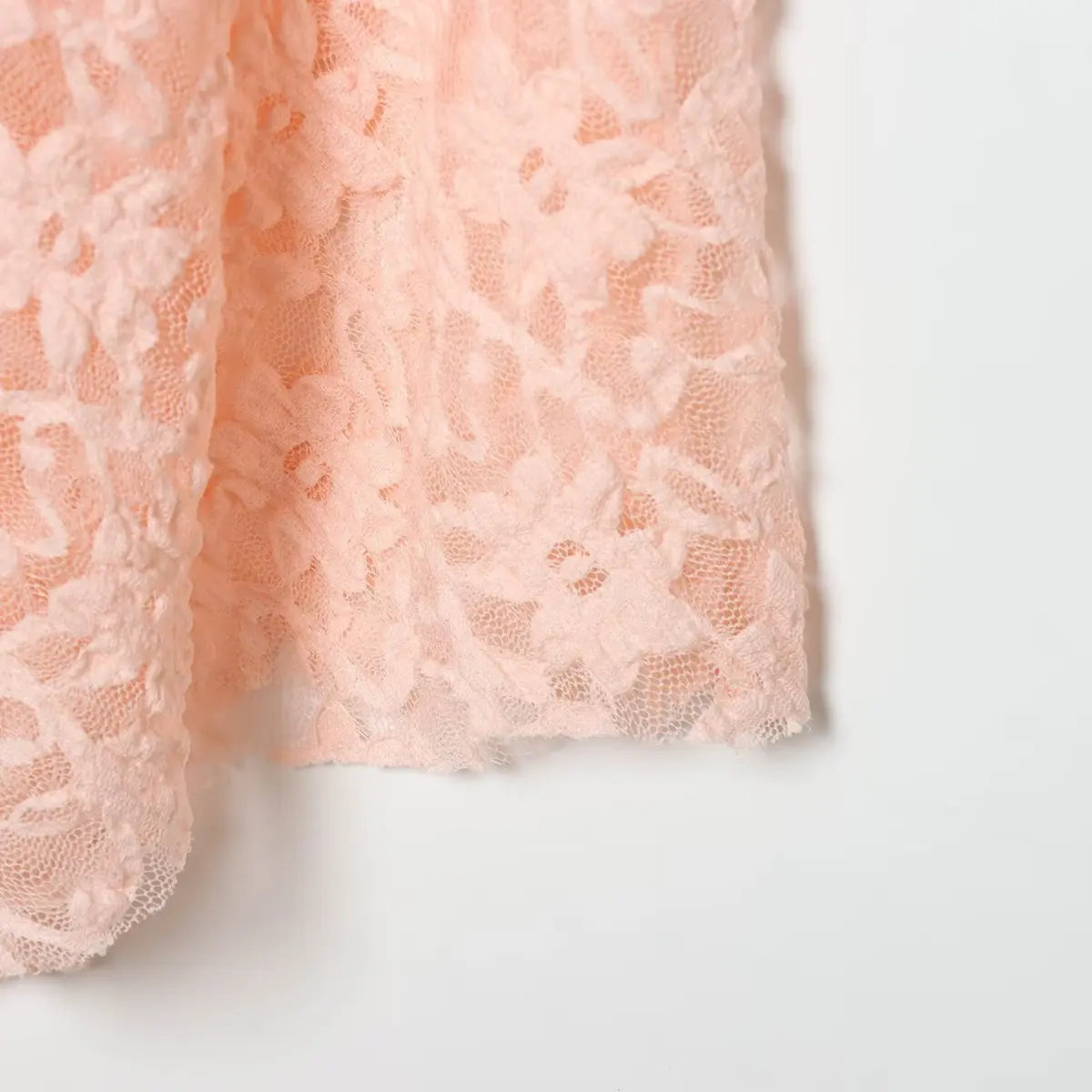 Close-up of the asymmetrical hem on the blush pink lace dress, showing the floral lace pattern