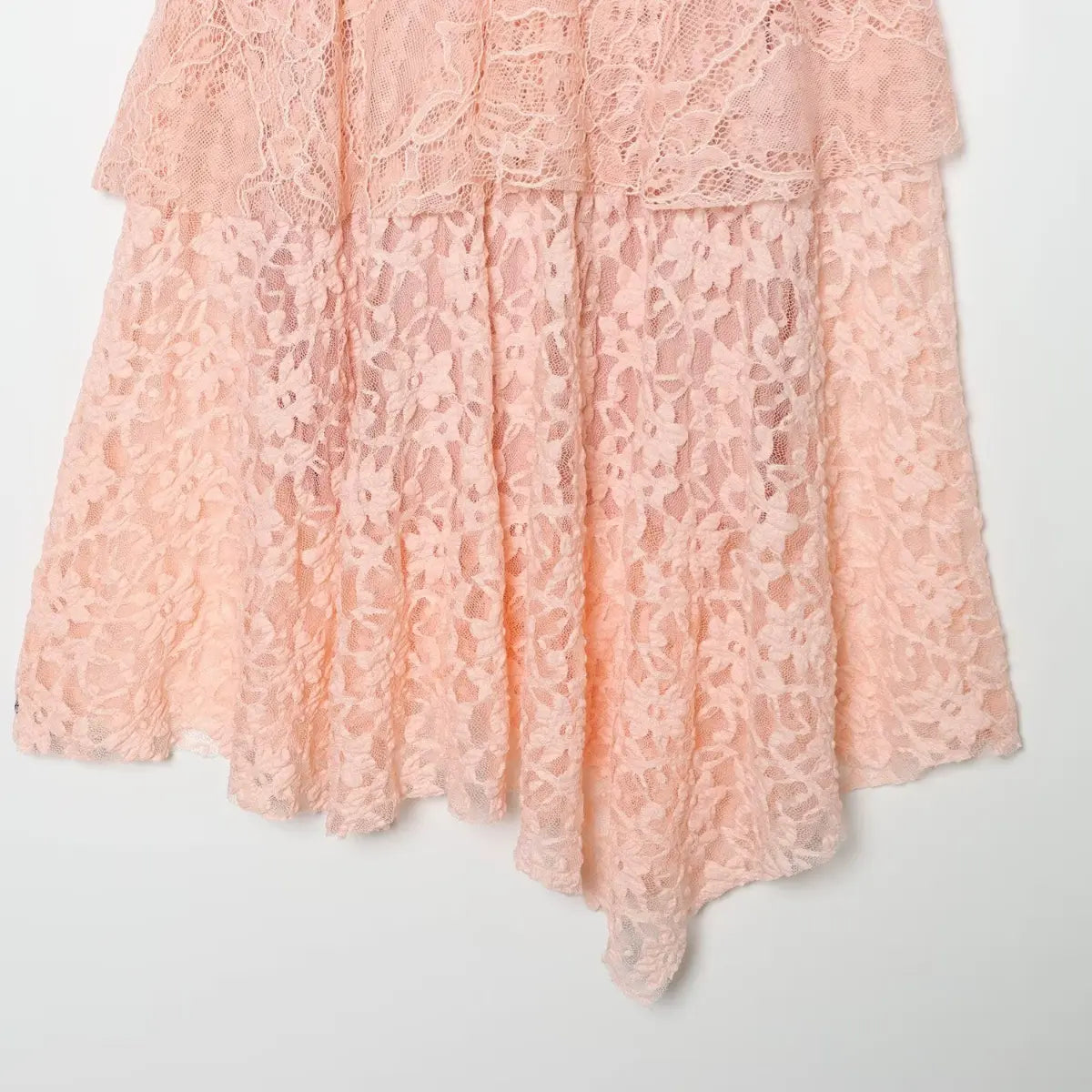 Close-up of the asymmetrical hem on the blush pink lace dress, showing the floral lace pattern