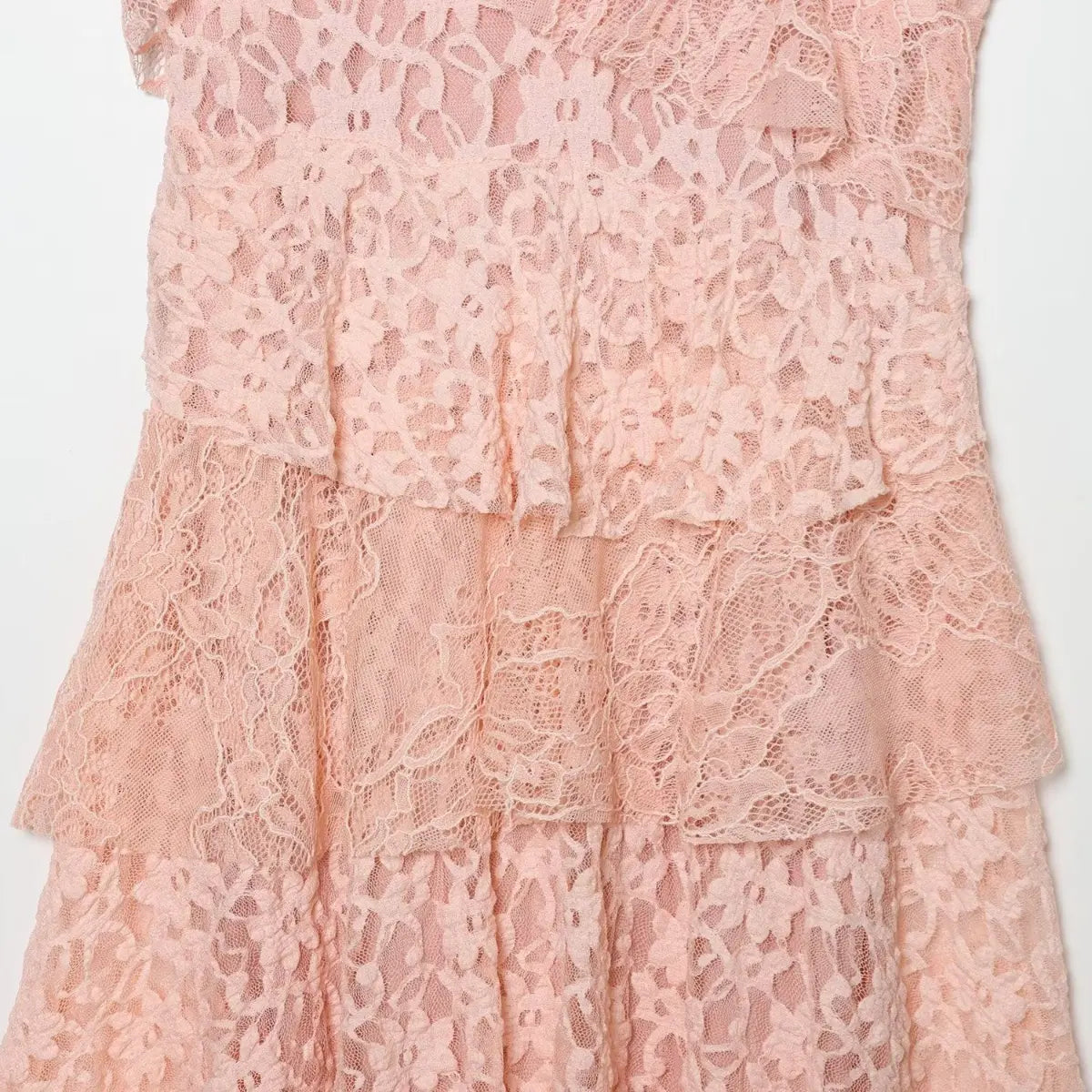 Close-up of the tiered skirt on the blush pink lace dress, showing the floral lace pattern and ruffled layers