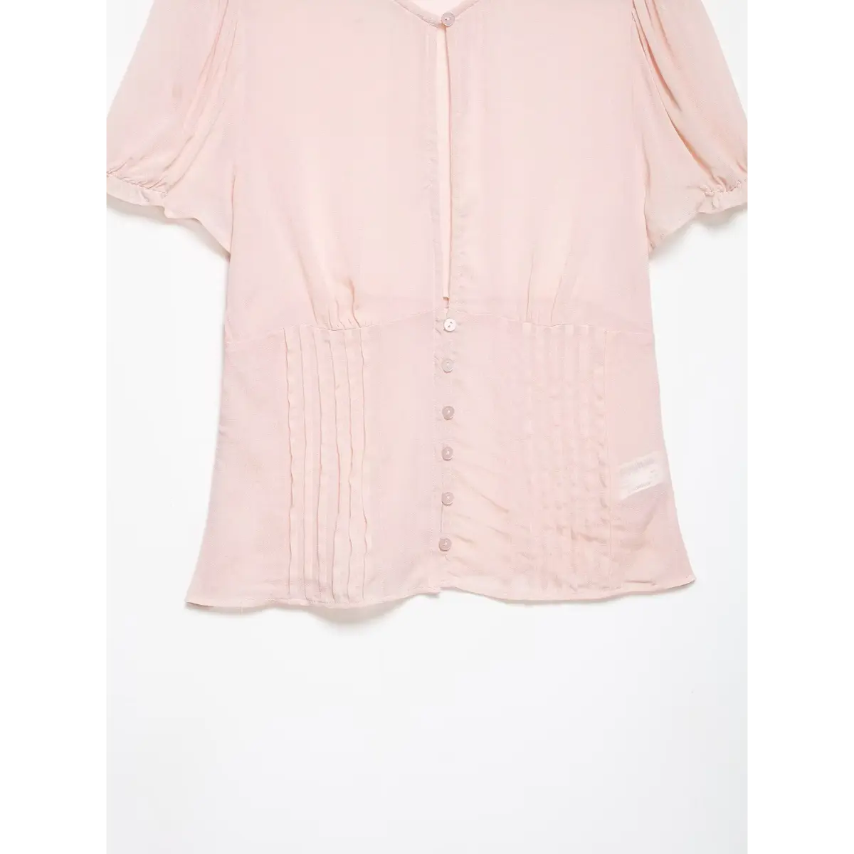 Detail shot of the pleated waist and button closure on the blush pink blouse.