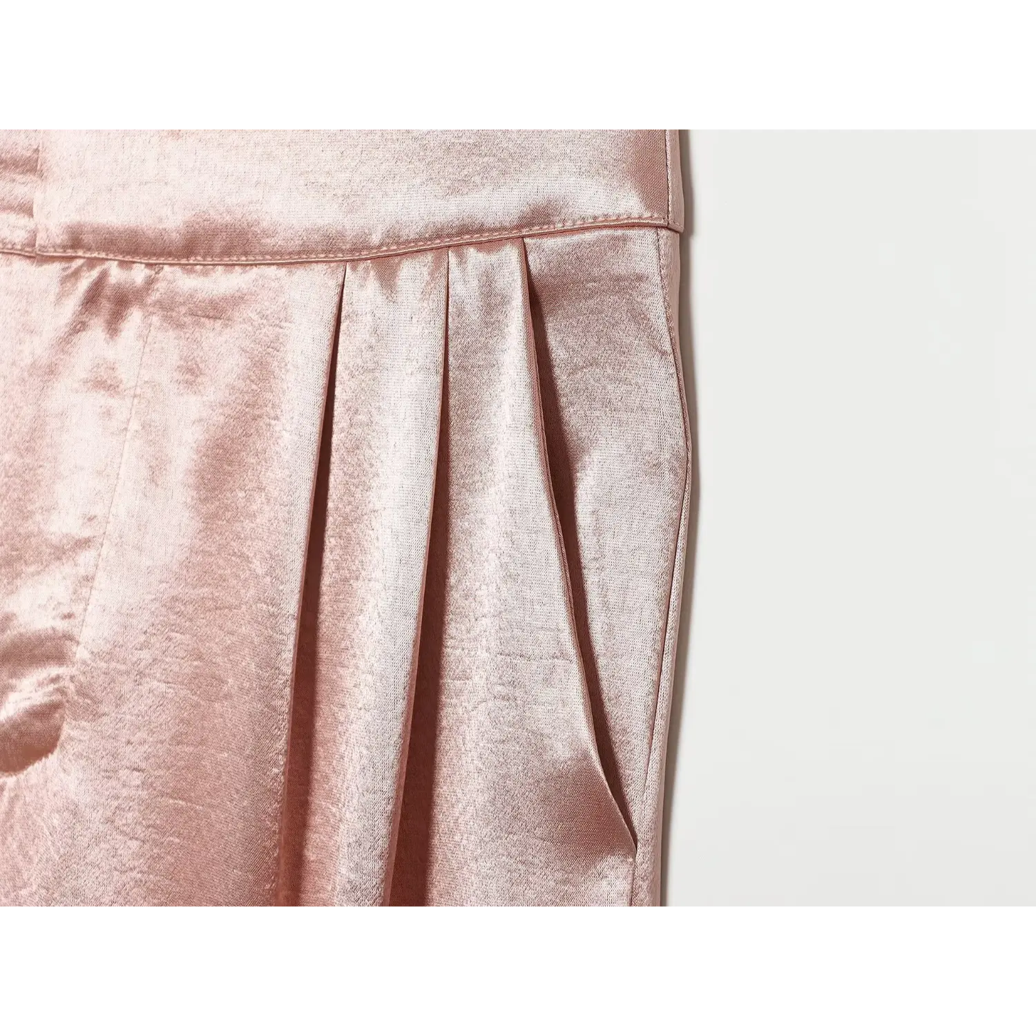 Close‑up front pleat and side pocket detail of blush pink satin tapered pants