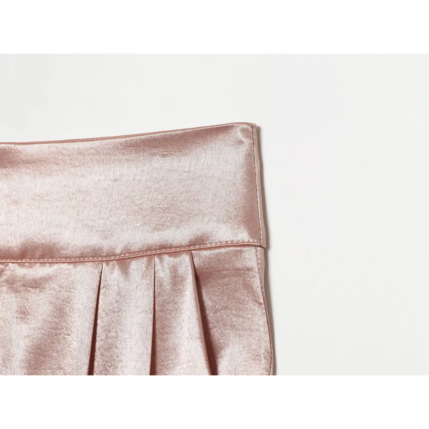 Close‑up shot waistband stitching and pleat detail of blush textured satin trousers