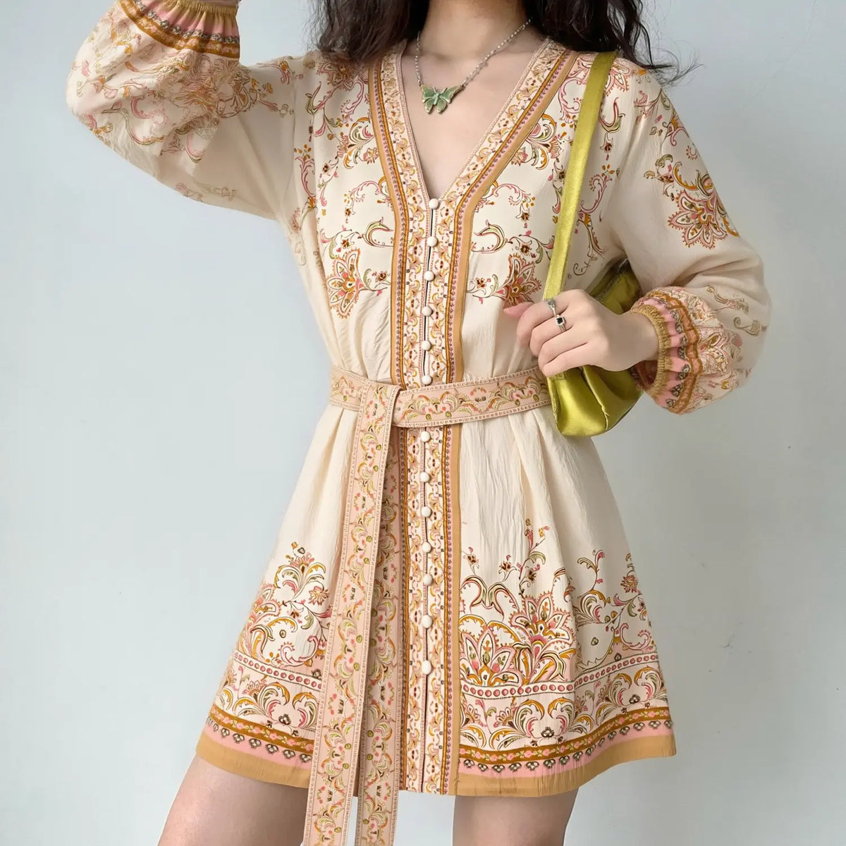 Female model wearing cream boho paisley v‑neck mini dress with matching waist tie belt, long balloon sleeves