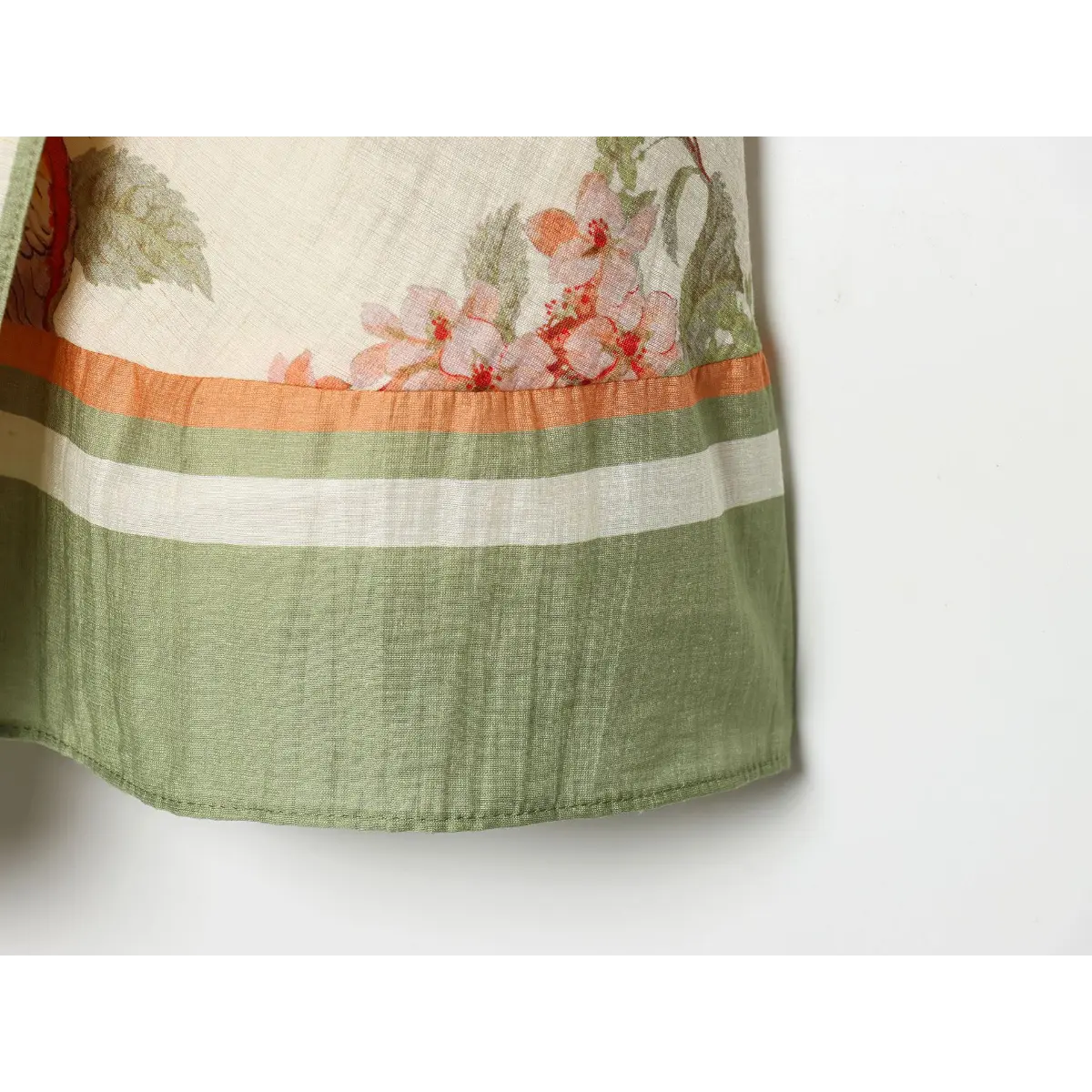 Fabric macro detail, textured crinkle linen material with peach floral print, triple color block hem trim in green, white and orange.