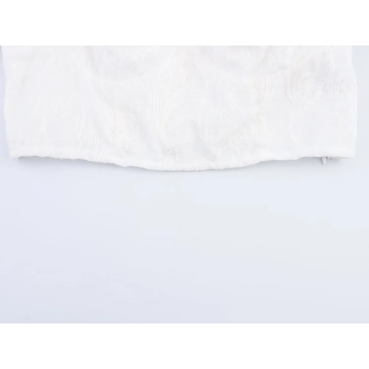 Close-up of elastic bottom hem on white embroidered cropped blouse