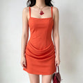 Model wearing a bright orange corset-style mini dress with a draped front detail and wide straps, carrying a red handbag.