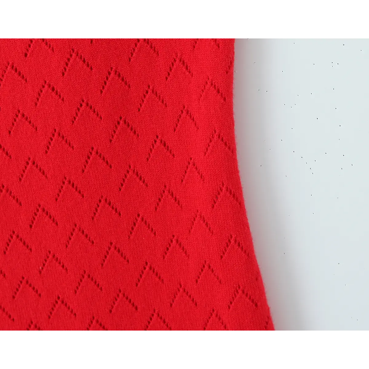 Macro close-up of scarlet hollow chevron knit fabric, breathable openwork textured knit material detail.