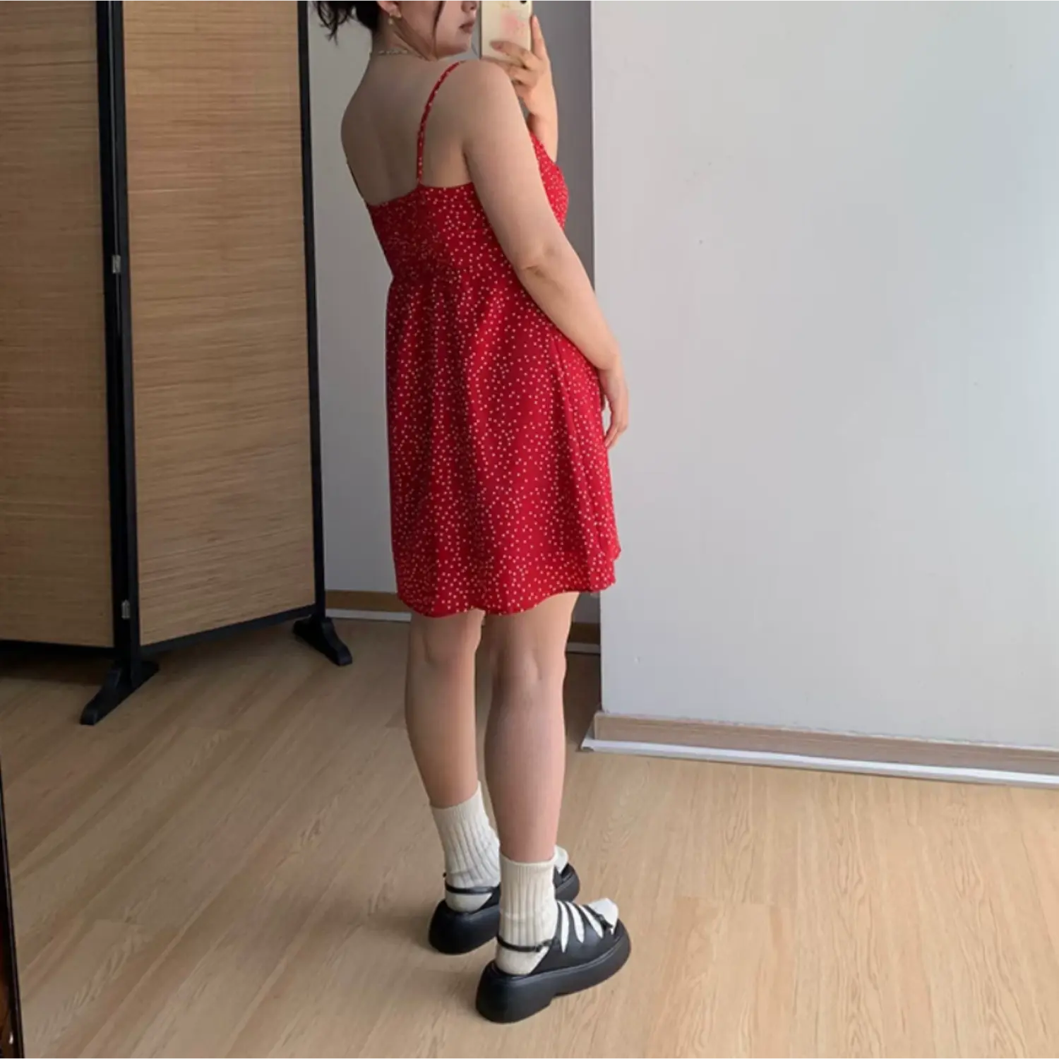Three-quarter back indoor mirror shot of red white polka dot mini dress, full elastic smocked rear waist panel, thin adjustable spaghetti straps, loose A-line mini skirt hem