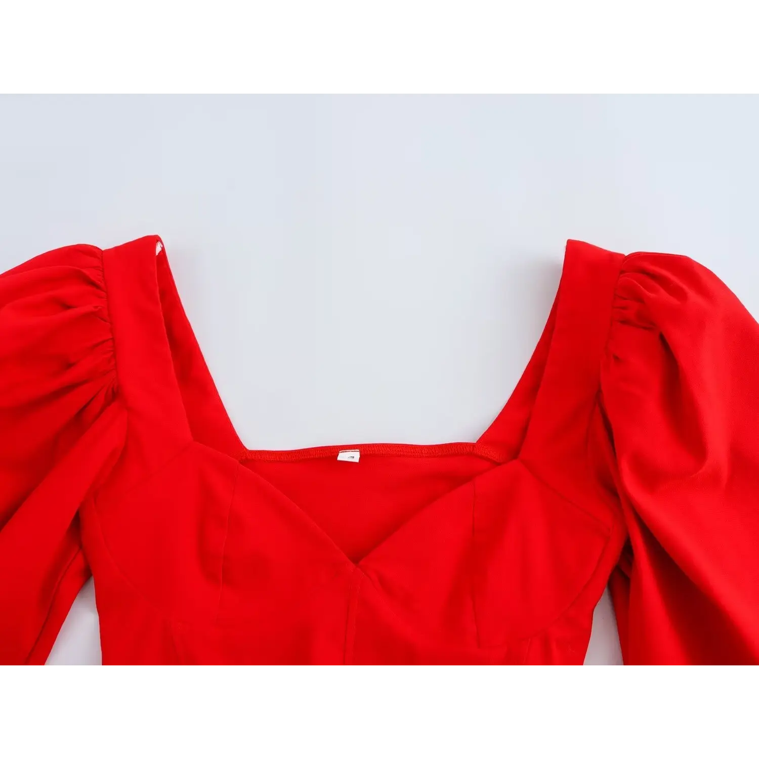 Full partial view of square neckline, inner label, and puff shoulder on bright red corset crop to