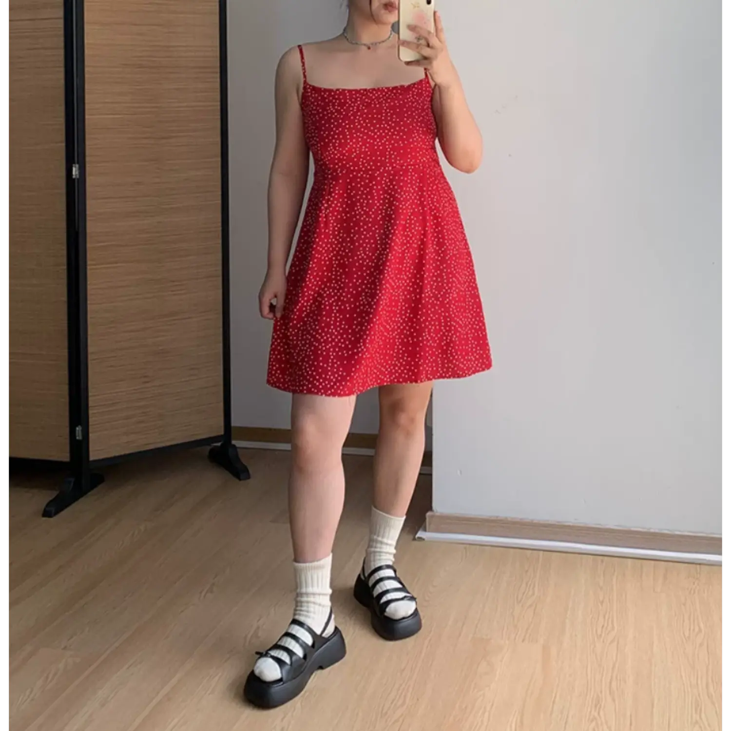 Indoor mirror full front shot of vivid red mini slip dress covered in small white polka dots, thin adjustable straps, A-line flared skirt, paired with white crew socks and black multi-strap platform sandals