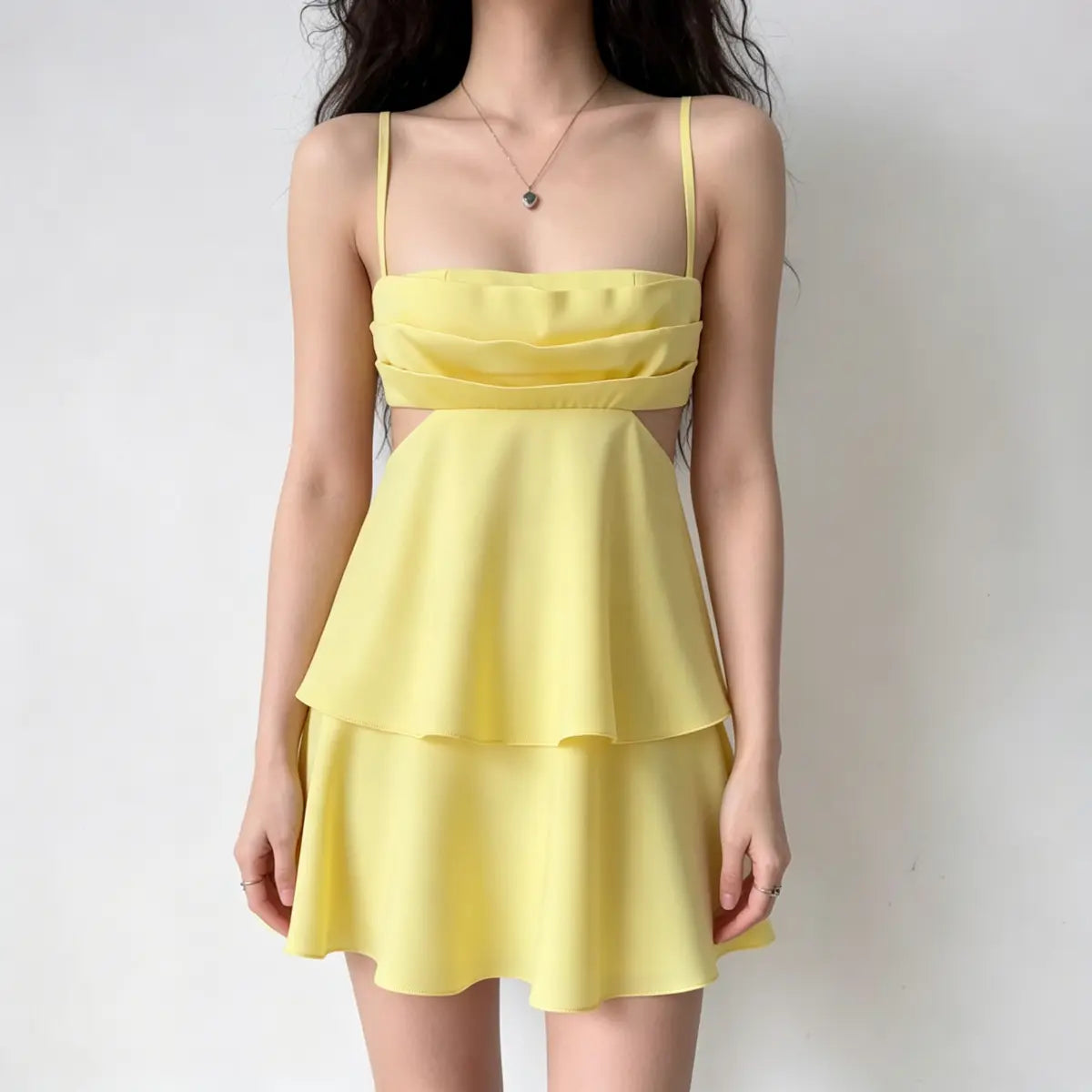 Model wearing a bright yellow spaghetti-strap mini dress with tiered ruffles at the bust and skirt, and side waist cutouts.