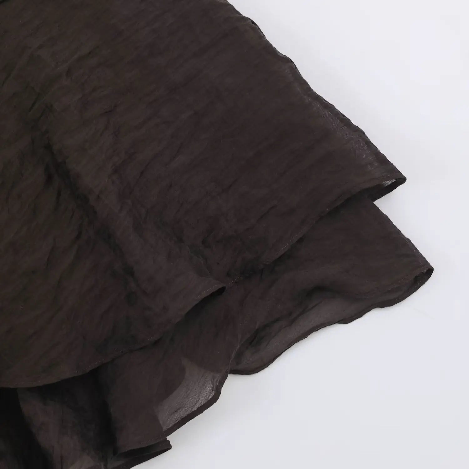 Skirt hem macro shot of dark brown halter dress, neat finished edge on crinkled semi-sheer woven fabric