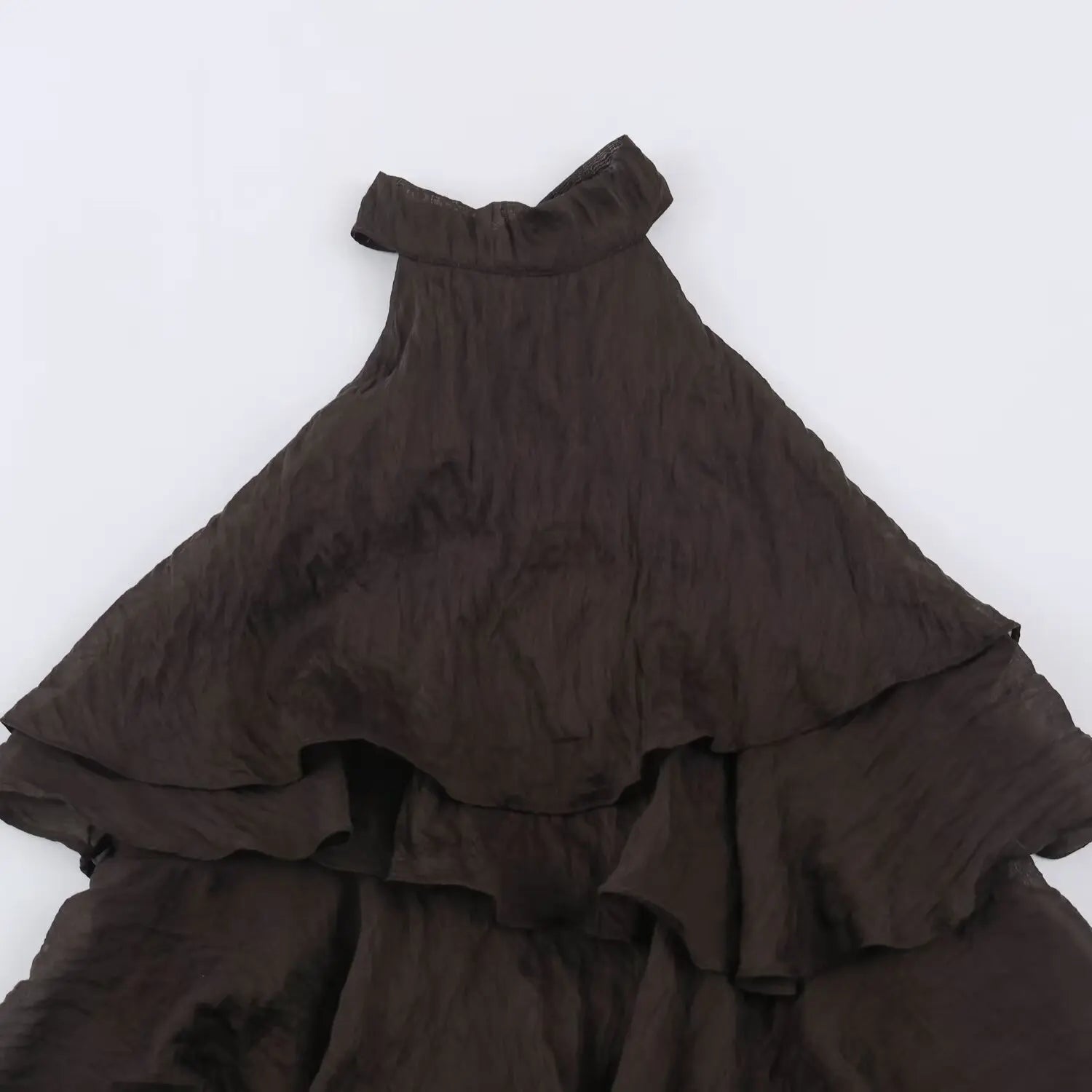 Partial close-up of dark brown halter dress neckline, stand halter collar and upper waterfall ruffle layers, wrinkled woven fabric texture