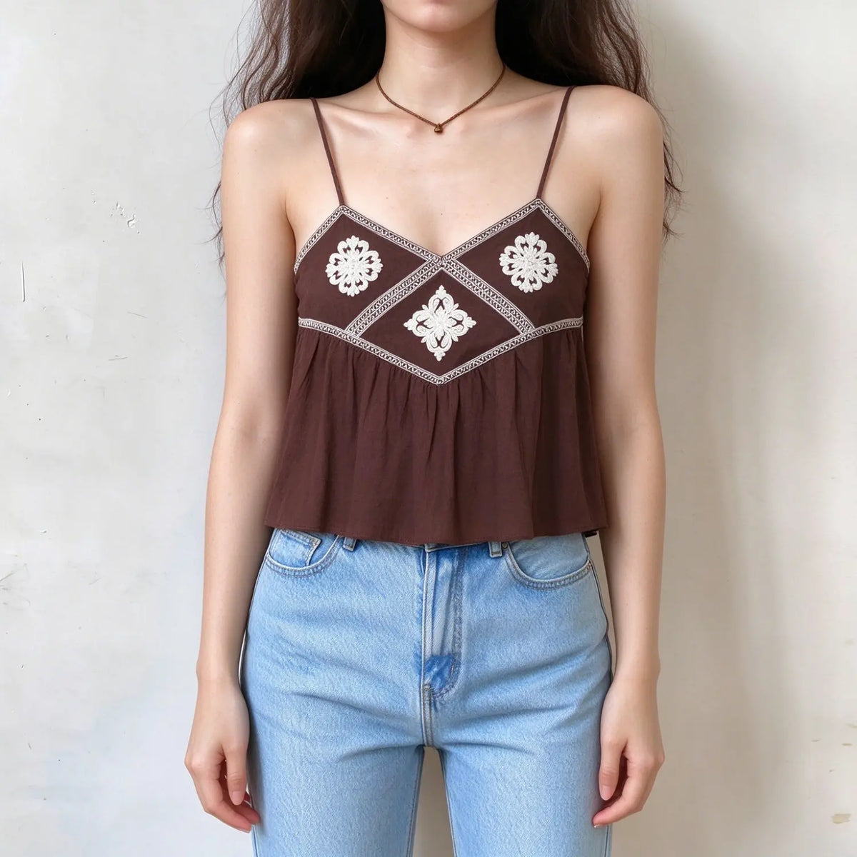Model wearing brown embroidered tassel tie cami top with jeans, front view