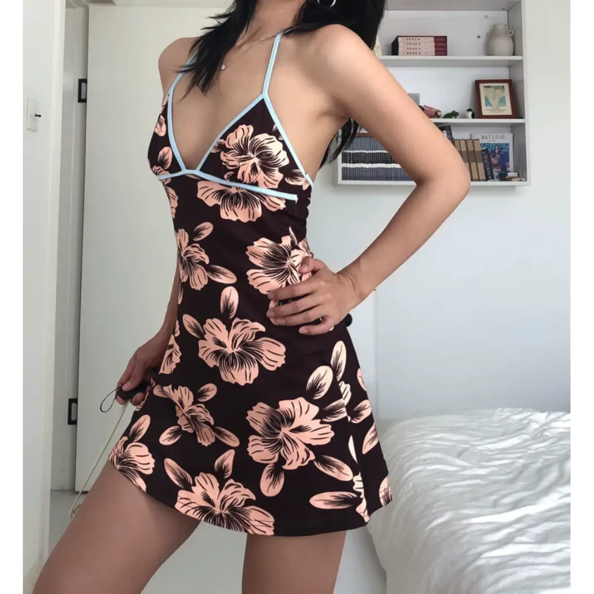 Angled view of a woman wearing a brown halter mini dress with pink hibiscus floral print and light blue trim, posed with one hand on her hip.