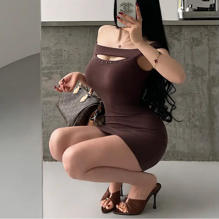 A woman in a squatting pose wearing a brown ribbed off-shoulder mini dress with stud details, styled with brown heels and a Louis Vuitton bag.