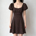 Model wearing a brown and pink polka dot mini dress with a square neckline, puff sleeves, and a buttoned bodice.