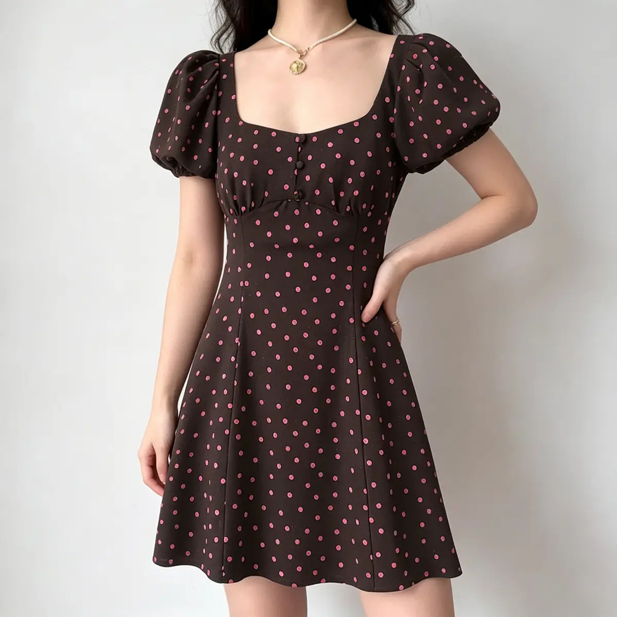 Model wearing a brown and pink polka dot mini dress with puff sleeves, featuring a square neckline, button placket, and fitted A-line silhouette.