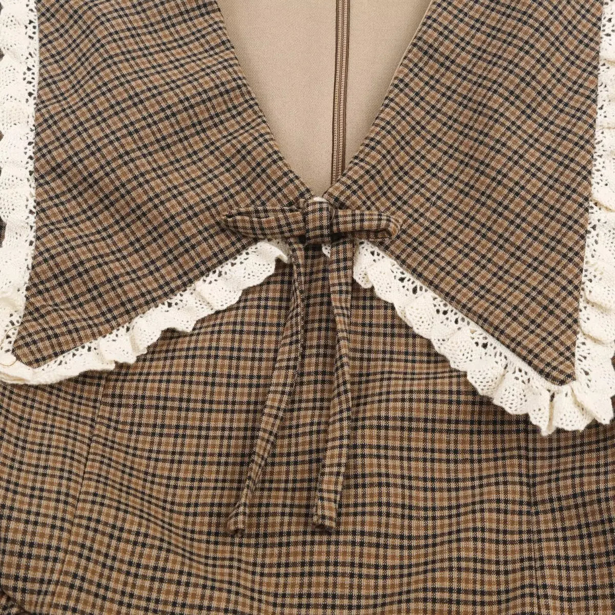  Close-up of the front sailor collar on a brown plaid dress, showing the white lace trim and fabric bow detail.