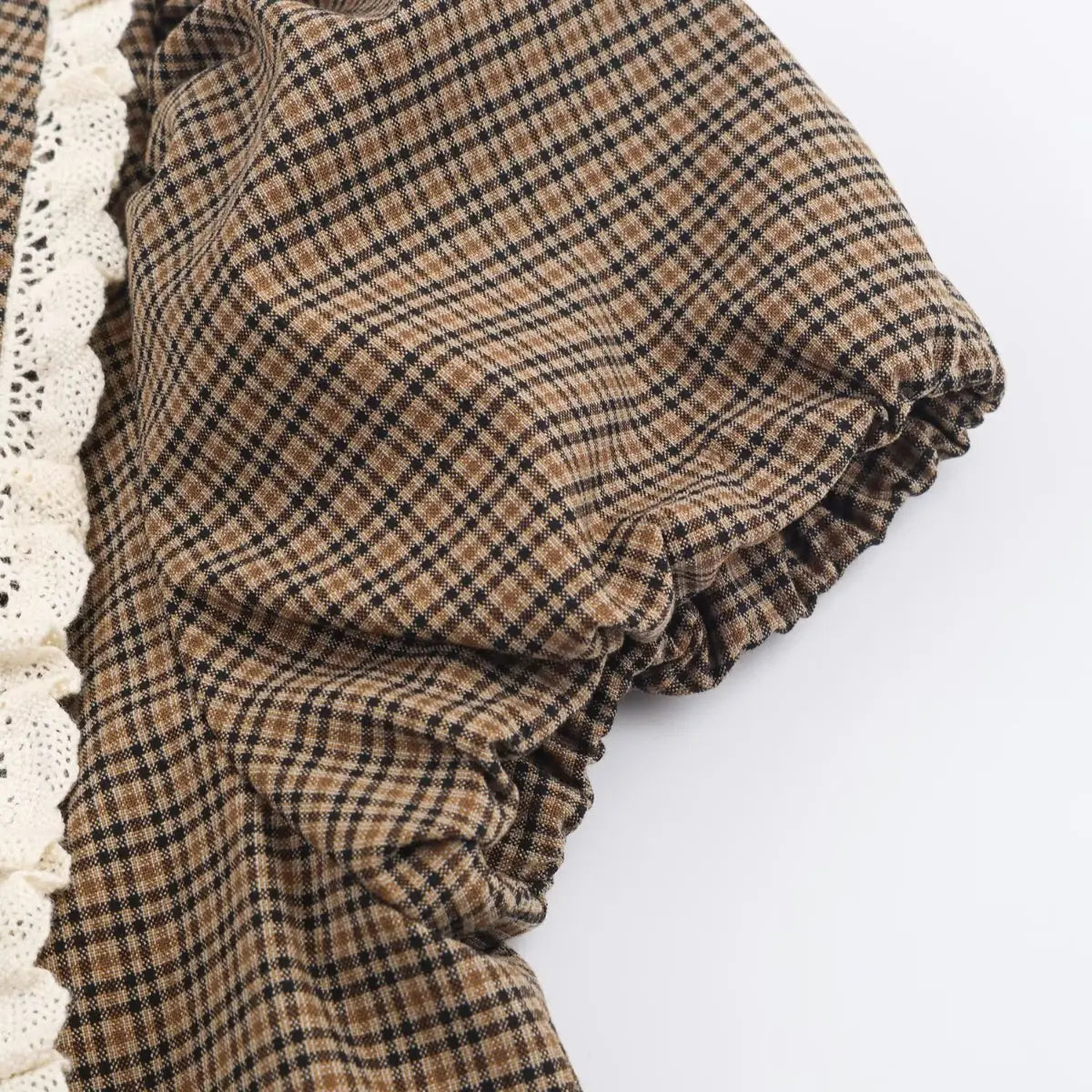 Close-up of the gathered puff sleeve on a brown plaid dress, showing the elasticated edge and white lace trim.