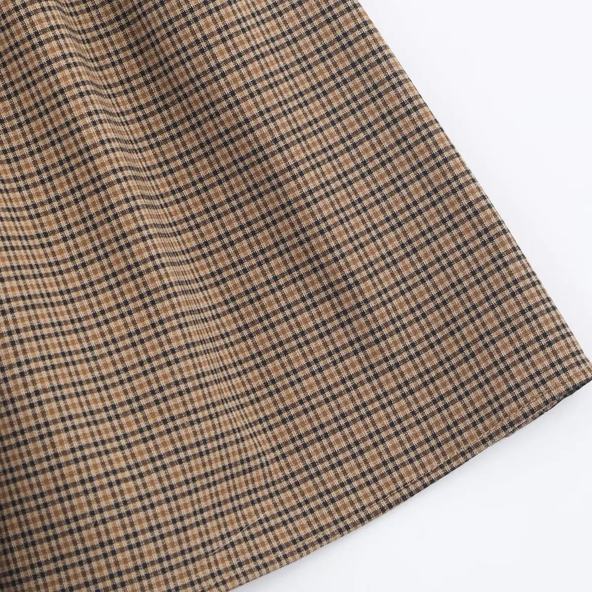Close-up of the finished skirt hem on a brown, black, and beige plaid dress, showing the fabric drape.