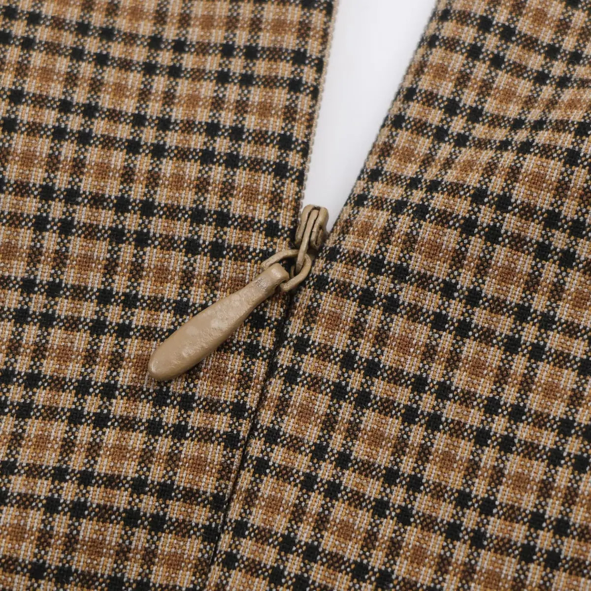 Close-up view of the antique-style metal zipper pull on a brown, black, and beige plaid dress.
